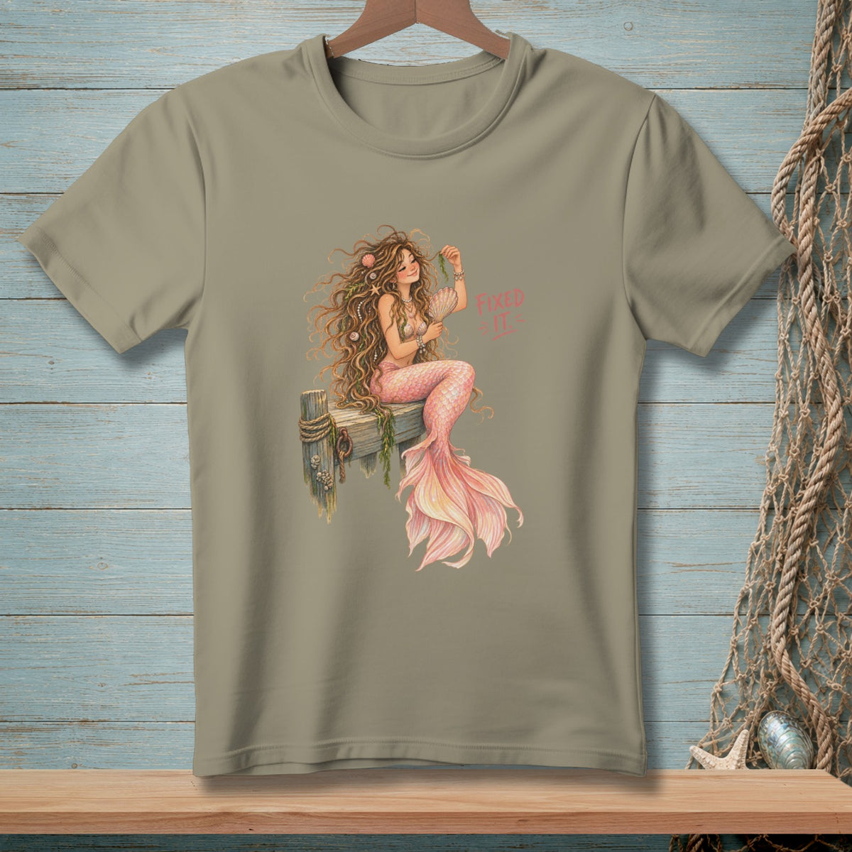 T-shirt with a mermaid sitting on a wooden post, holding seaweed, with text "Fixed It".
