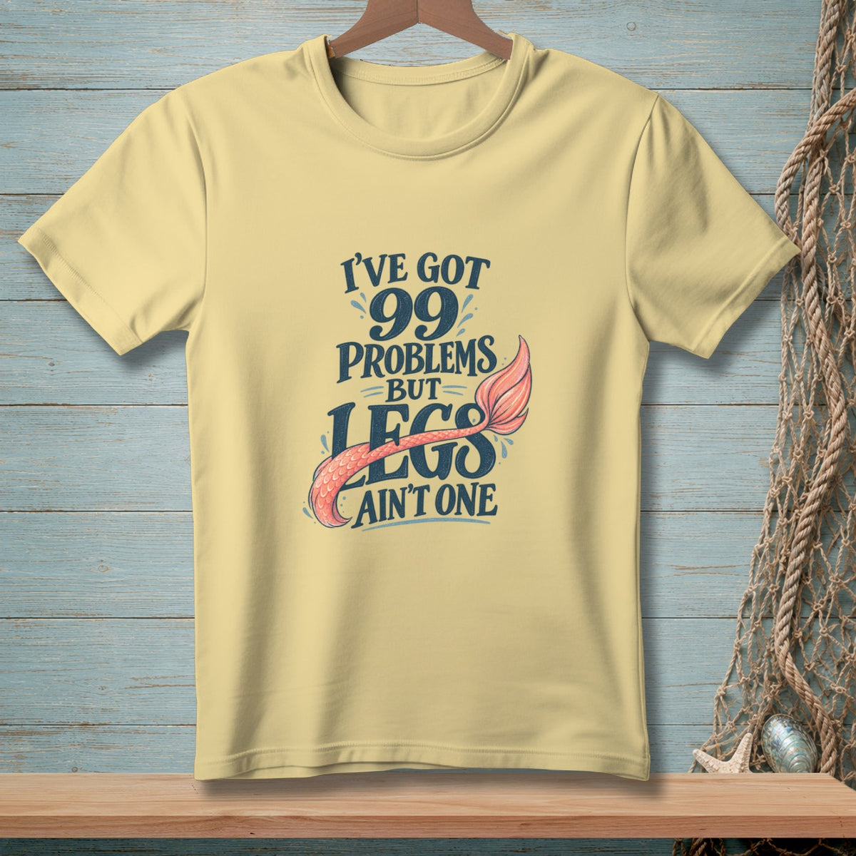 Pale yellow t-shirt with "I've got 99 problems but legs ain't one" text and mermaid tail.