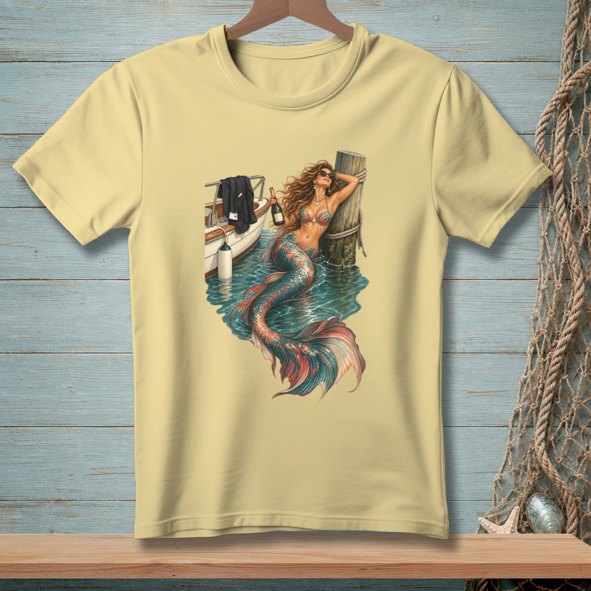Yellow t-shirt featuring a mermaid leaning against a wooden post with a boat and champagne.