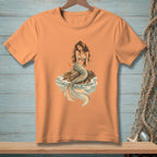 Peach t-shirt with a drawing of a mermaid sitting on a rock by the sea.