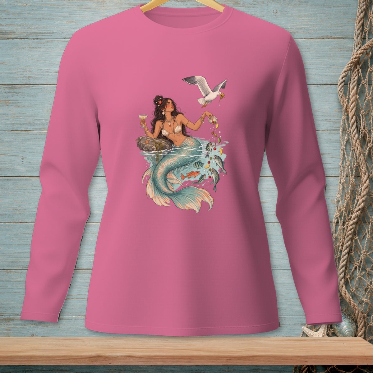 Illustration of mermaid with drinks, fish, and a seagull, printed on a pink long-sleeve shirt.