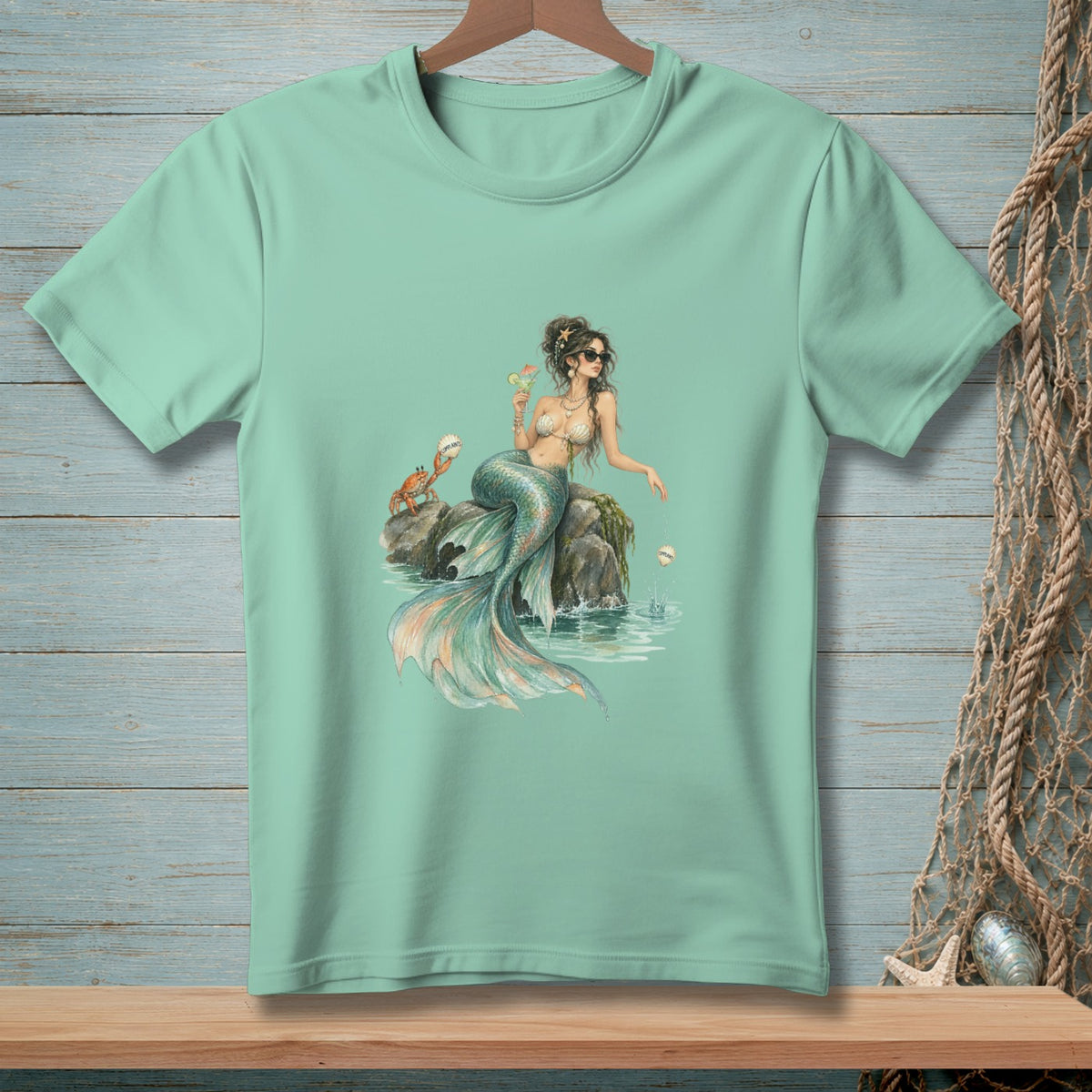 Mint green t-shirt with a watercolor illustration of a mermaid, a crab, and the ocean.