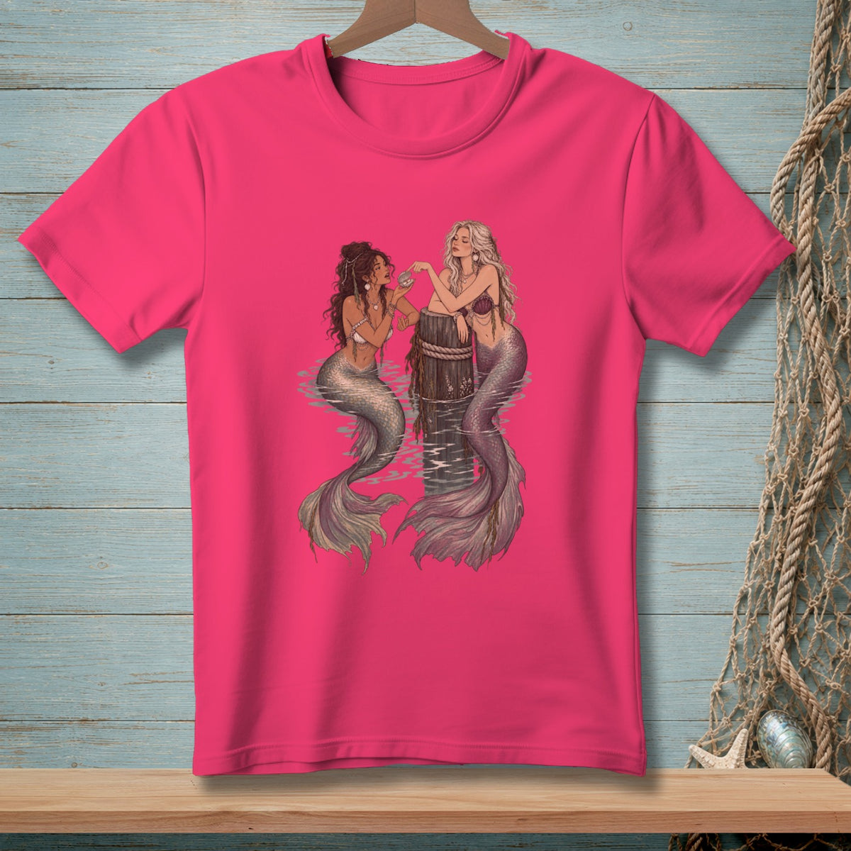 Two mermaids with tails pose near a wooden post in the water.