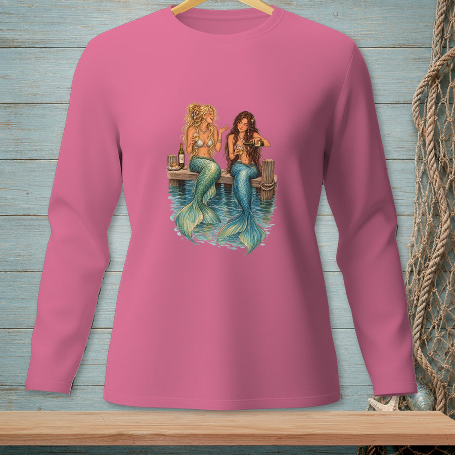 Two mermaids with green tails sit on a dock, drinking from wine glasses.