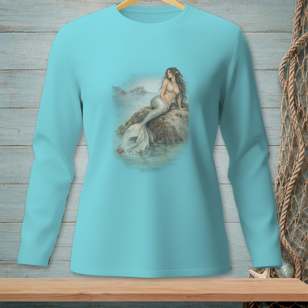 Mermaid sitting on a rock by the ocean with a crab nearby, printed on a teal long-sleeve shirt.