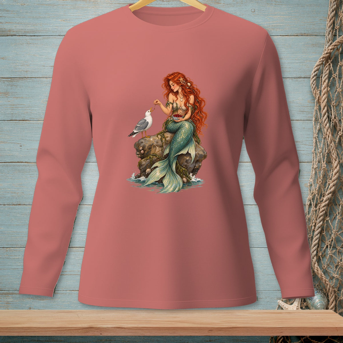 Mermaid feeding a seagull berries on a rock, on a rose-colored long-sleeved shirt.