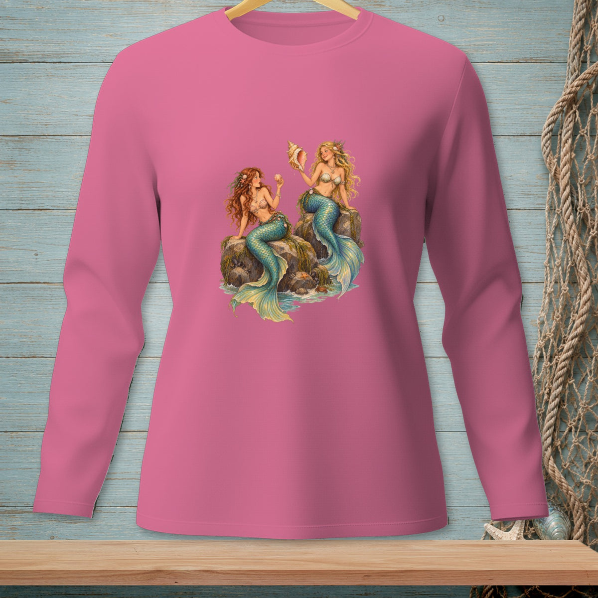 Pink long sleeve shirt with two mermaids sitting on rocks with a seashell.