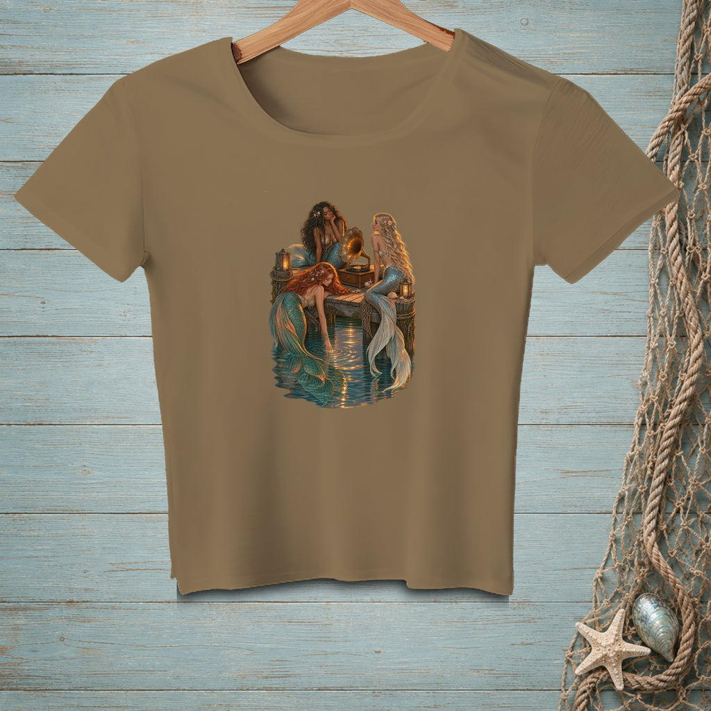 Three mermaids gather around a vintage phonograph on a dock.