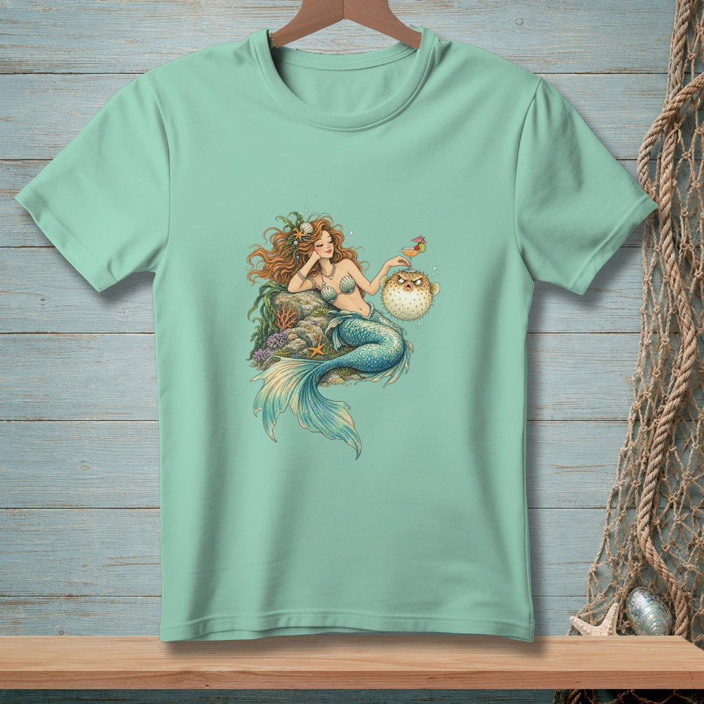 Mermaid holding a drink and interacting with a pufferfish on a light green t-shirt.