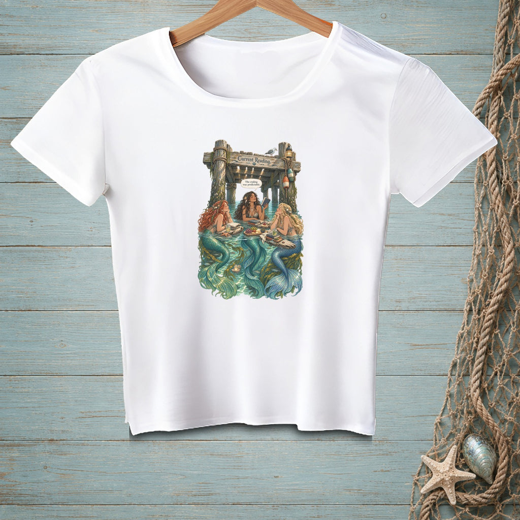 White t-shirt with three mermaids reading under a pier, with text "Current Reading".