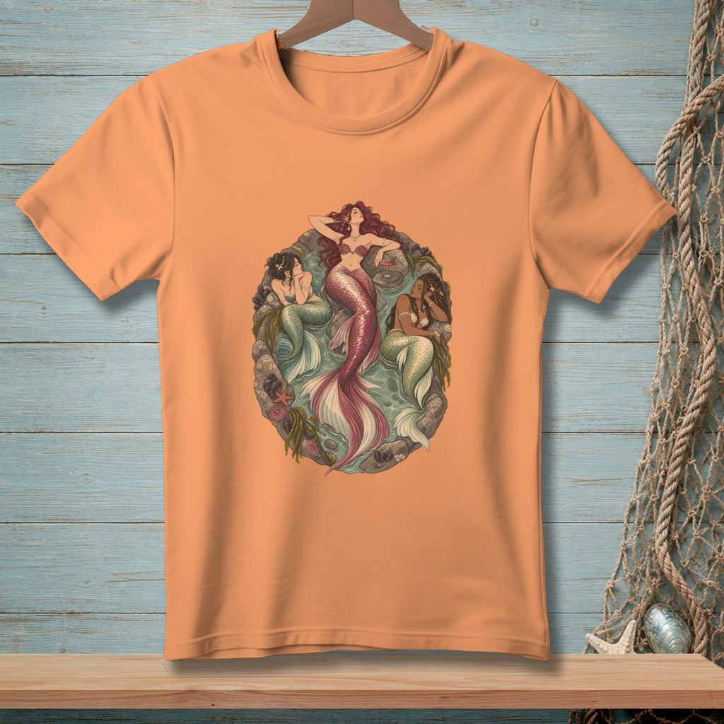 Orange t-shirt featuring three artistic mermaids with pink and green tails.