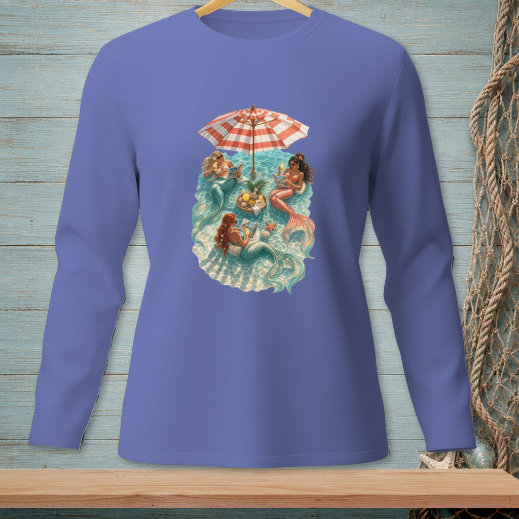 Mermaids lounging under a beach umbrella with drinks and fruit.