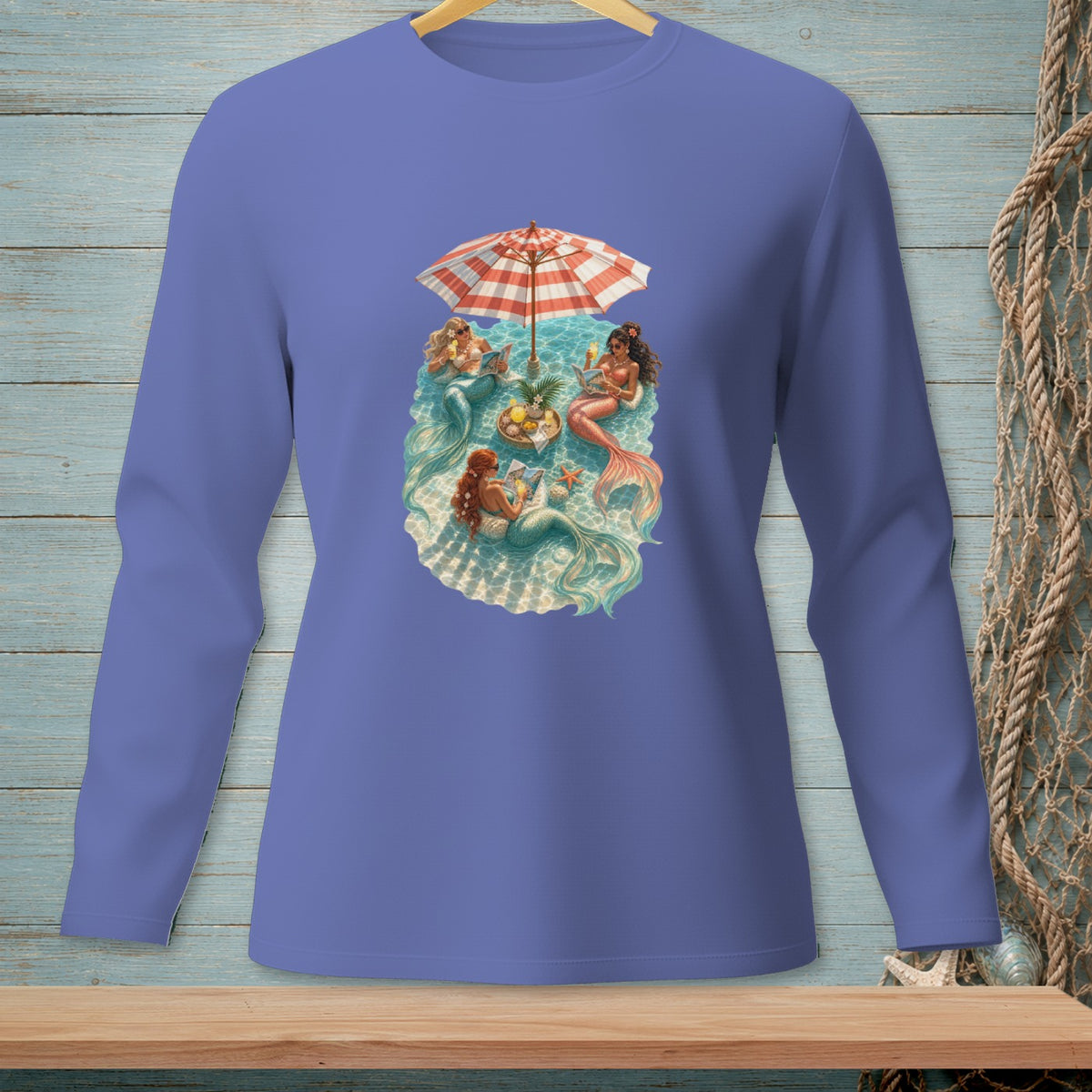 Mermaids lounging under a beach umbrella with drinks and fruit.