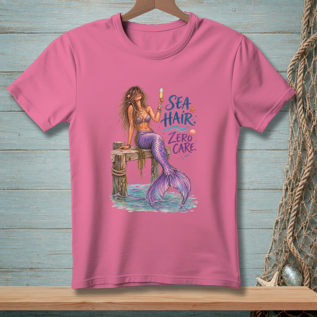 Pink t-shirt with mermaid illustration and text "Sea Hair Zero Care".