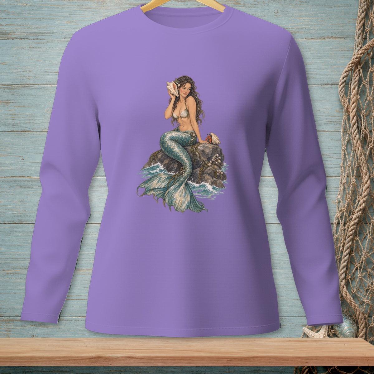 Lavender long-sleeve shirt with a mermaid illustration sitting on rocks by the sea.