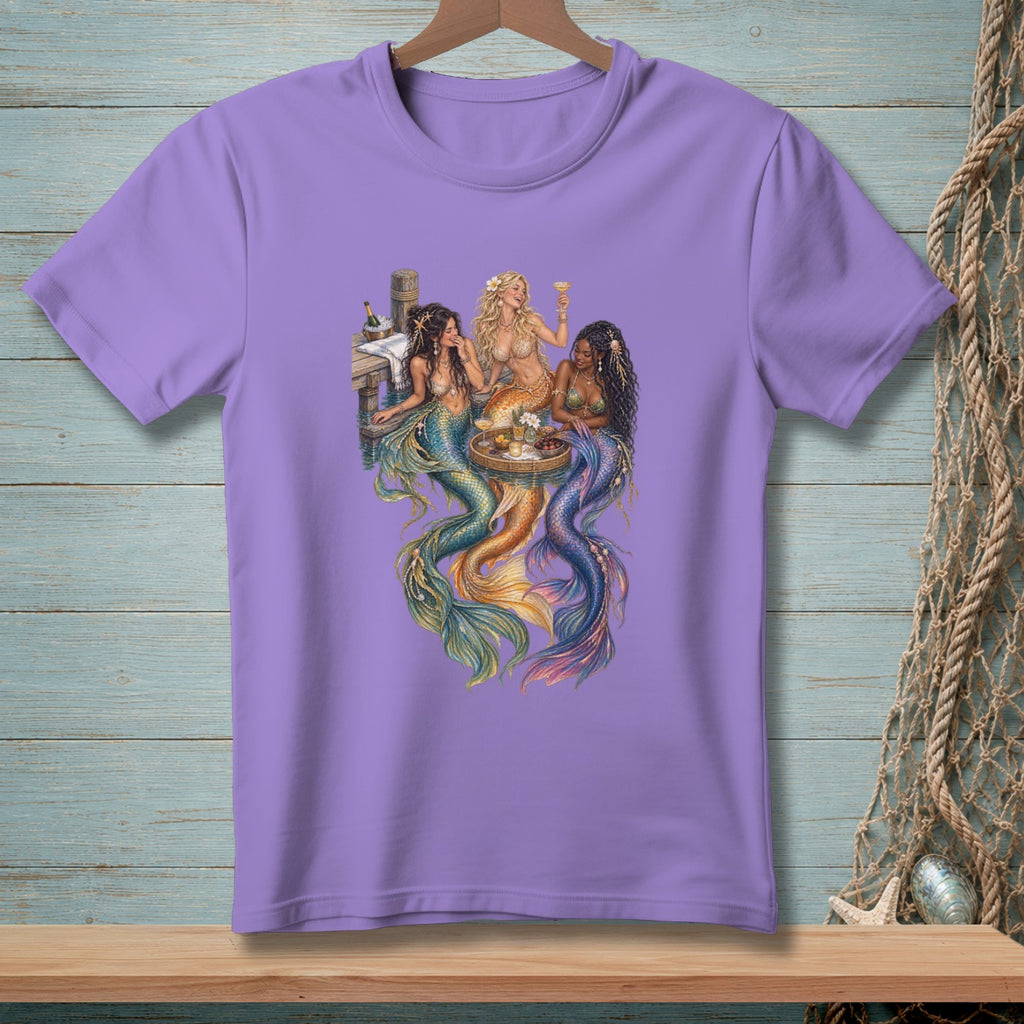 Three mermaids with colorful tails relax on a dock with drinks and a platter.