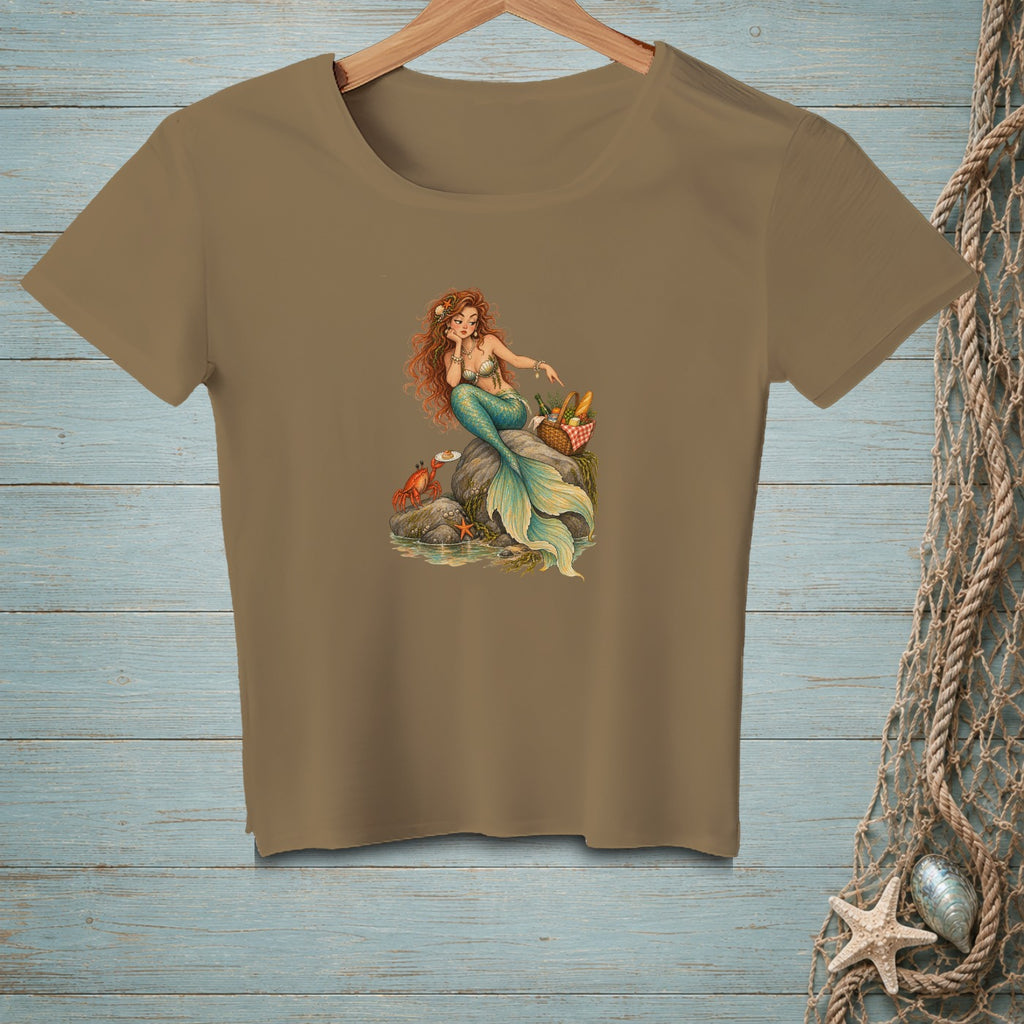 T-shirt with a brown graphic of a mermaid sitting on rocks with a crab and picnic basket.