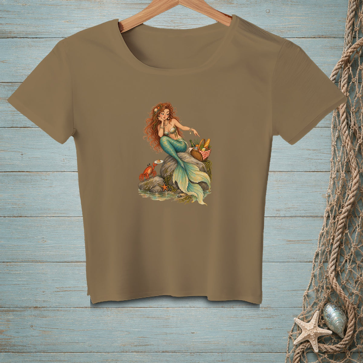 T-shirt with a brown graphic of a mermaid sitting on rocks with a crab and picnic basket.