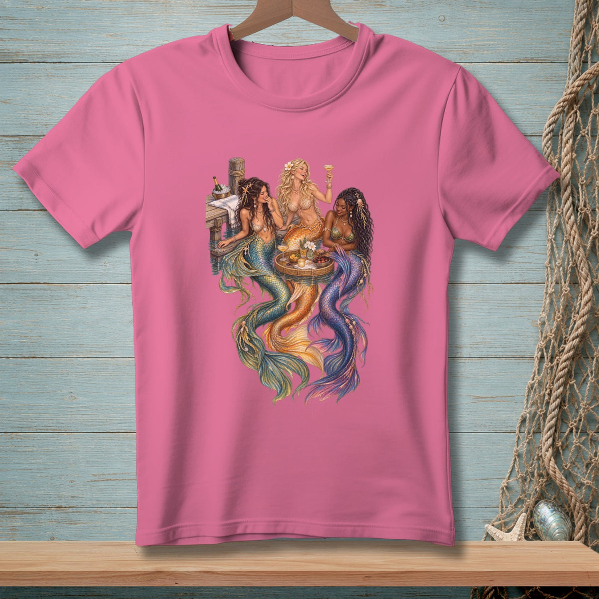 Three mermaids sit together on a dock, enjoying drinks and snacks.