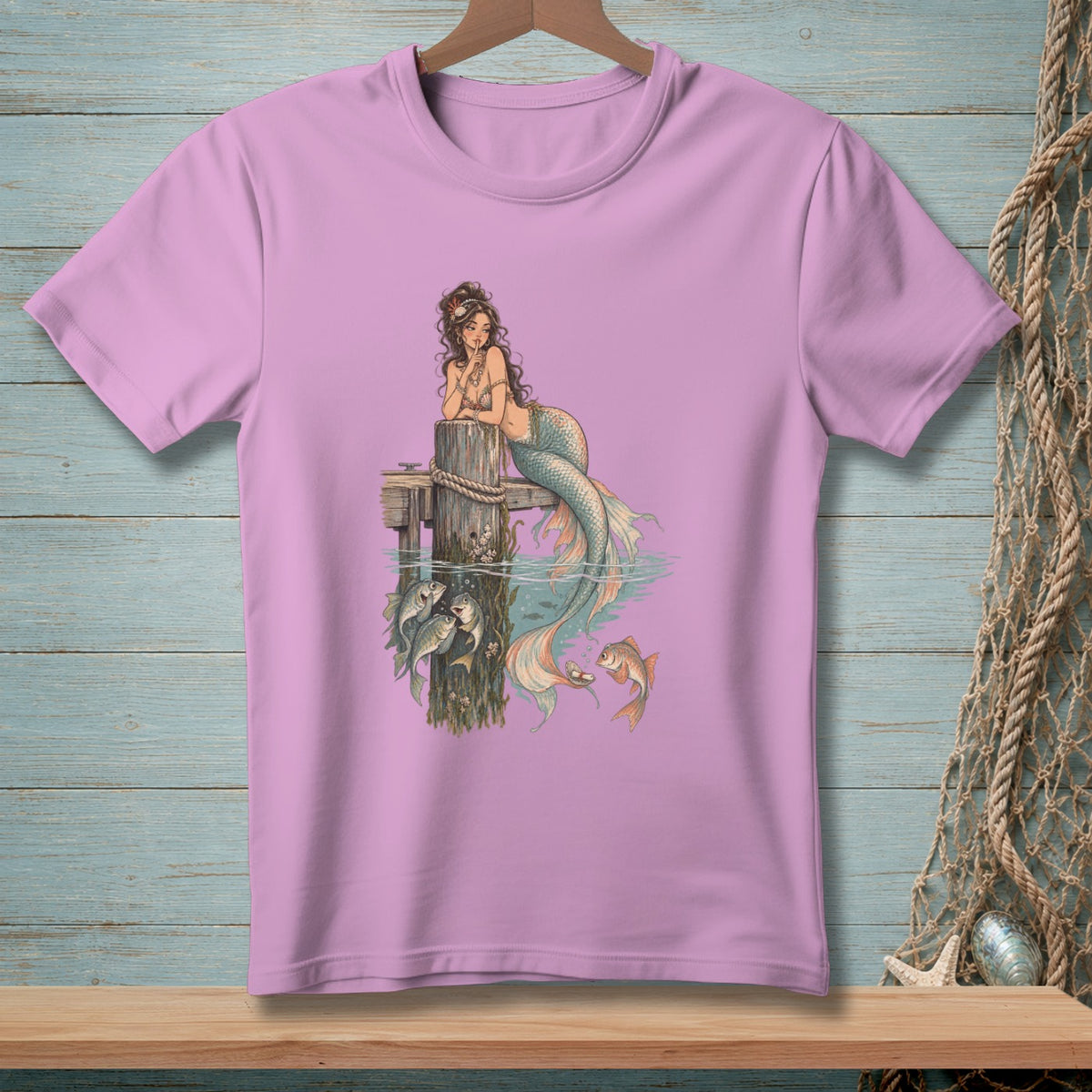 Lavender t-shirt with a vintage mermaid graphic and assorted fish by a pier.