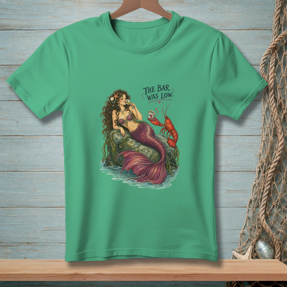 Mermaid sitting on rock with lobster, drinking, with text "The Bar Was Low."