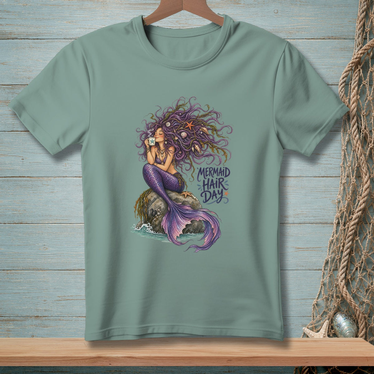 Teal t-shirt featuring a mermaid sitting on a rock, holding a mug, with text "MERMAID HAIR DAY."