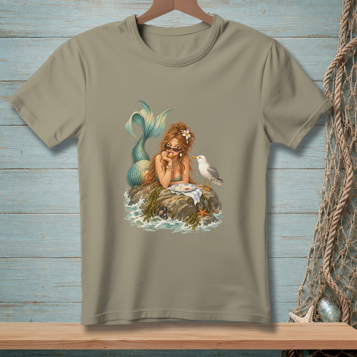 Mermaid with sunglasses sits on a rock with a plate of food and a seagull.