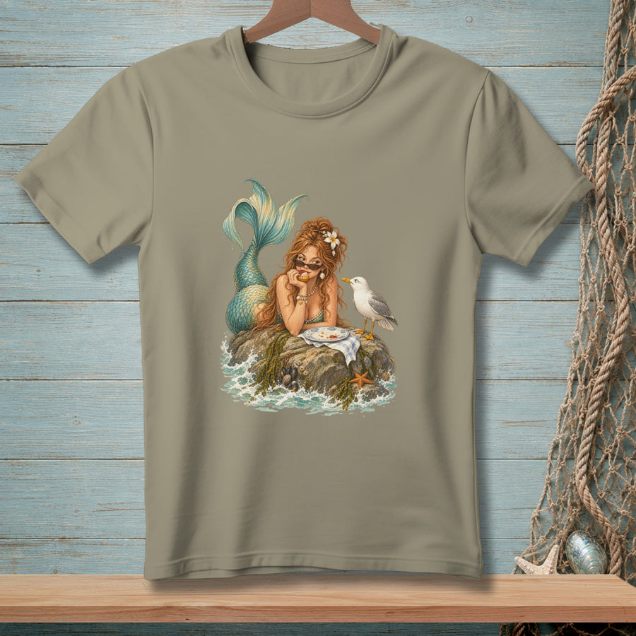 Mermaid with sunglasses sits on a rock with a plate of food and a seagull.