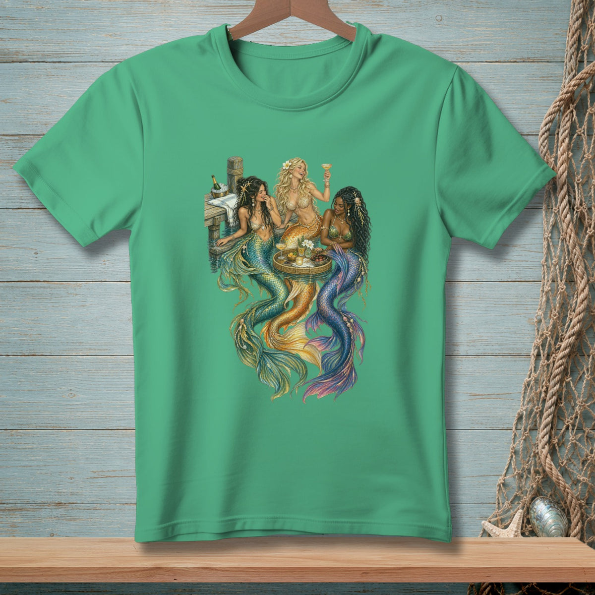Three mermaids sit at a table on a dock, holding drinks and surrounded by shimmering tails.