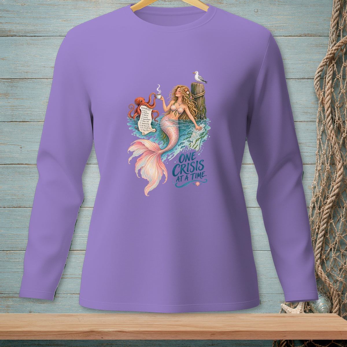 Purple long sleeve shirt with a mermaid, octopus, and seagull graphic that reads "One Crisis At A Time."