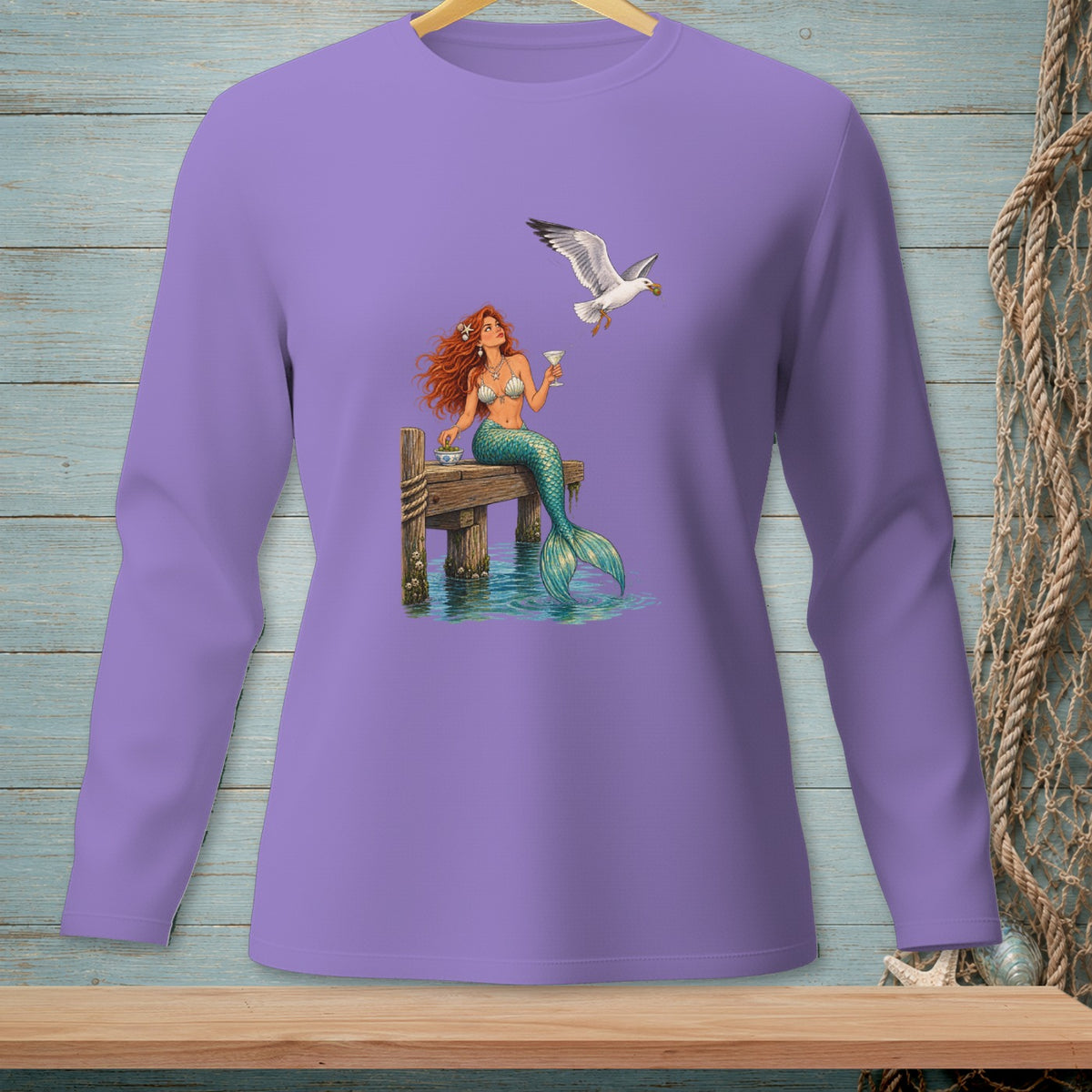 Purple long-sleeve shirt with a mermaid sitting on a dock with a drink and a seagull.