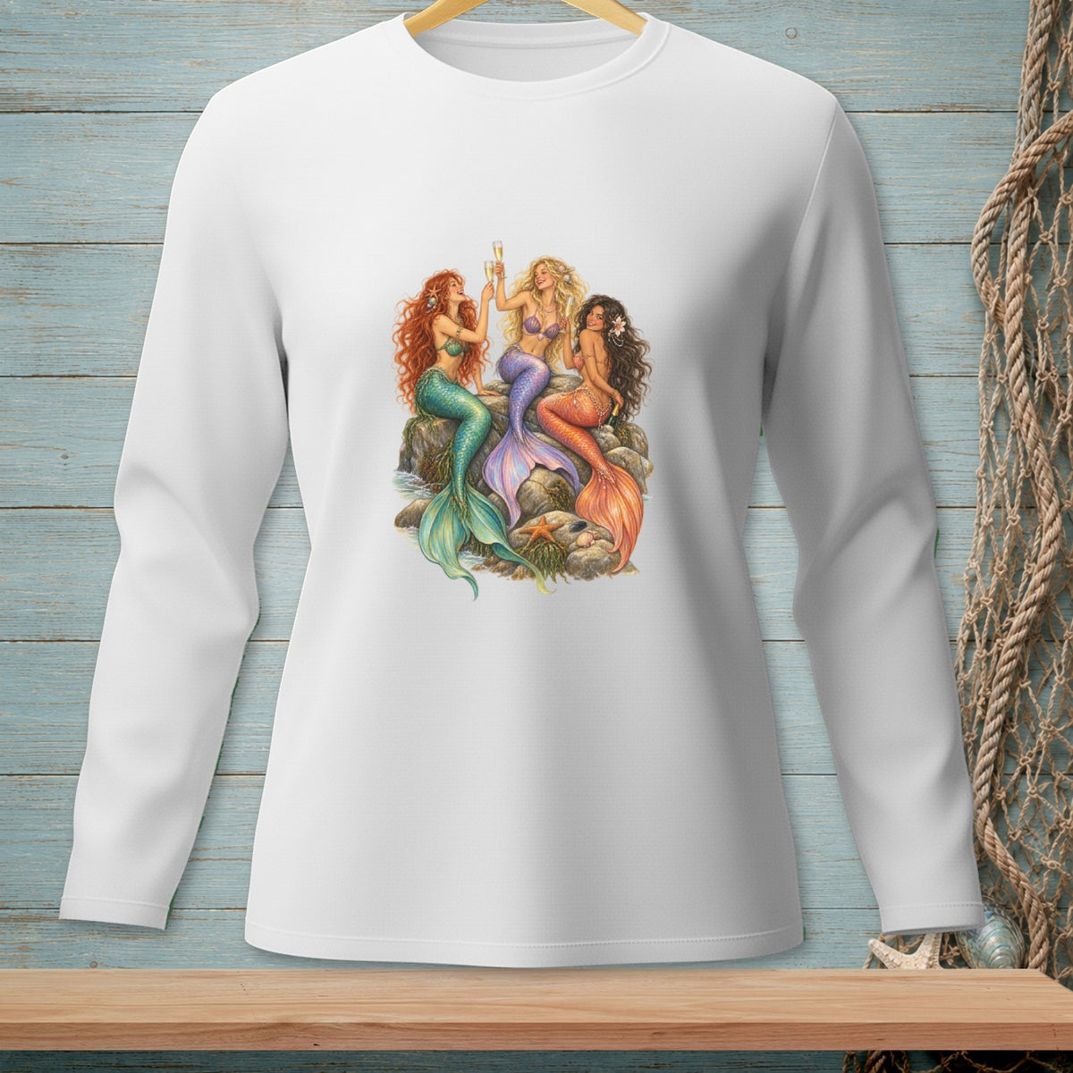 Three mermaids with colorful tails and glasses sit on rocks by the sea.