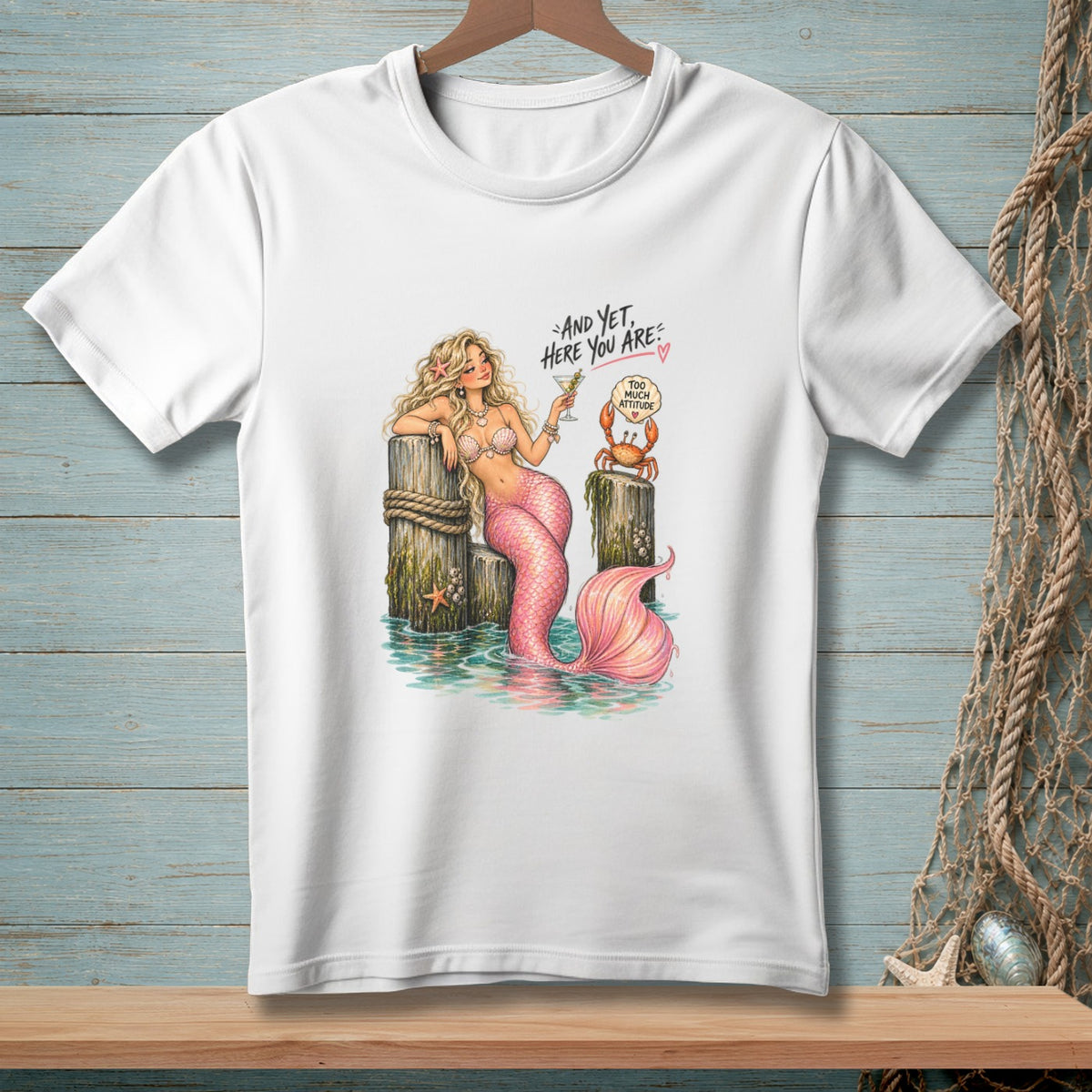 White t-shirt with a mermaid, crab, and text that reads "And Yet, Here You Are".