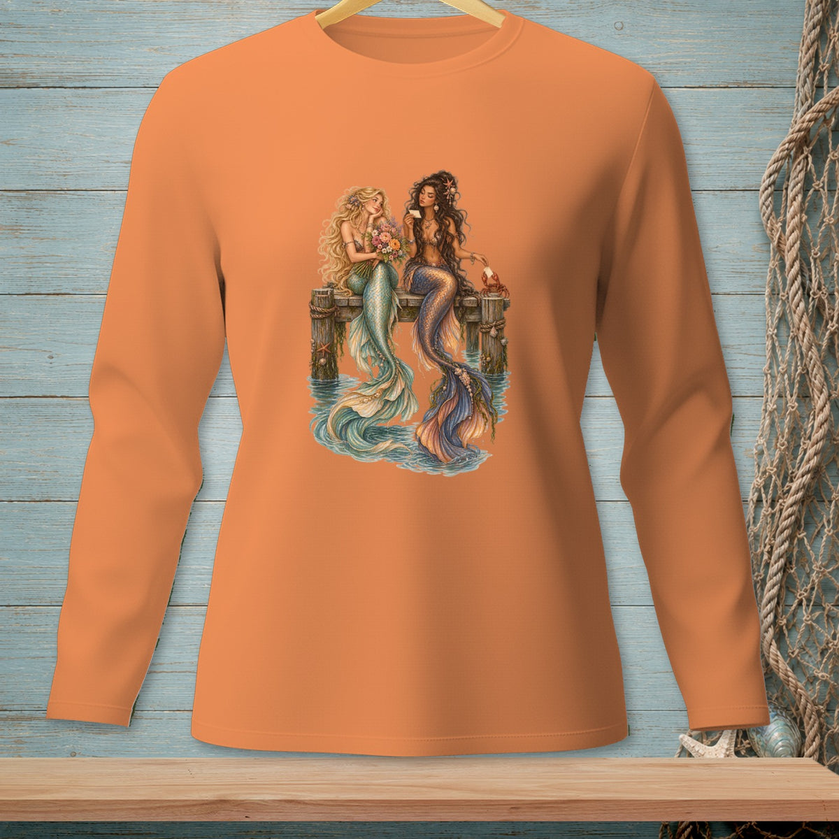 Two mermaids sit on a wooden pier, one with blonde hair holding flowers, the other with dark hair.