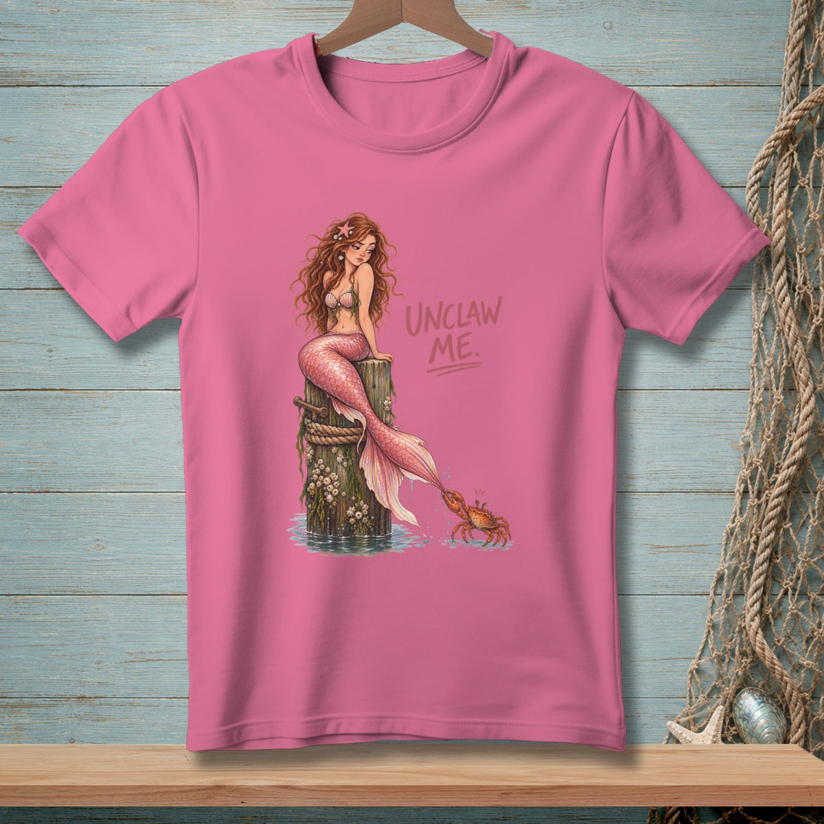 Pink t-shirt with mermaid illustration and "Unclaw Me." text.