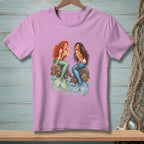 Two mermaids with colorful tails sit on rocks, one holding a pearl.