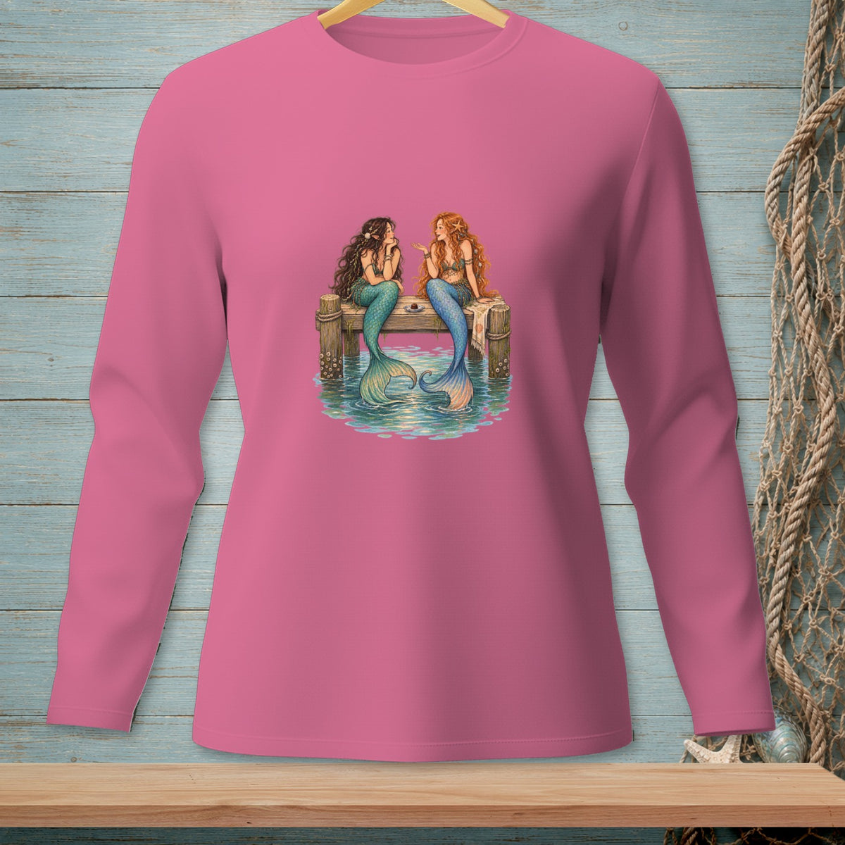 Pink long-sleeve shirt with two mermaids sitting on a dock.