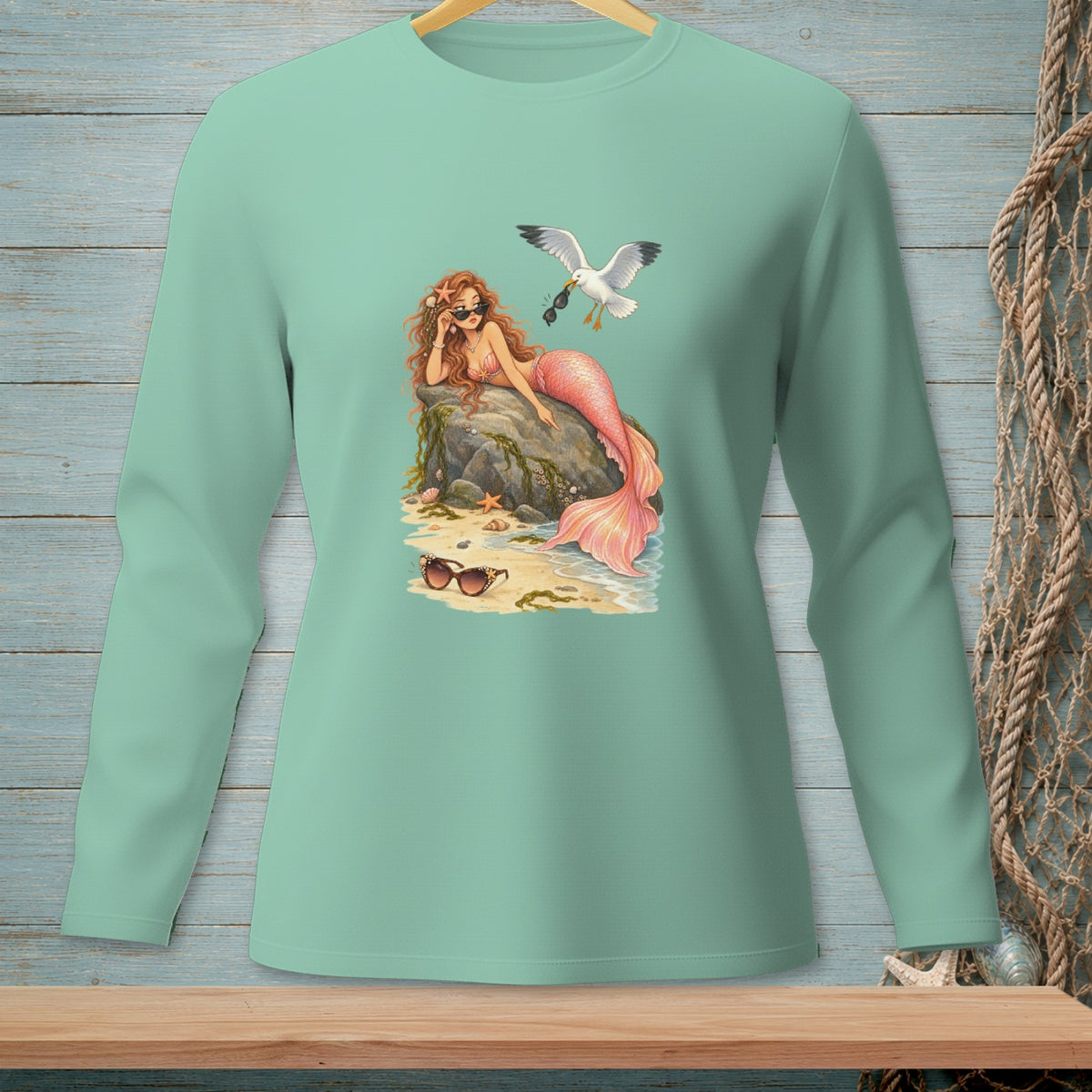 Mermaid with sunglasses and pink tail rests on rock; seagull flies by.