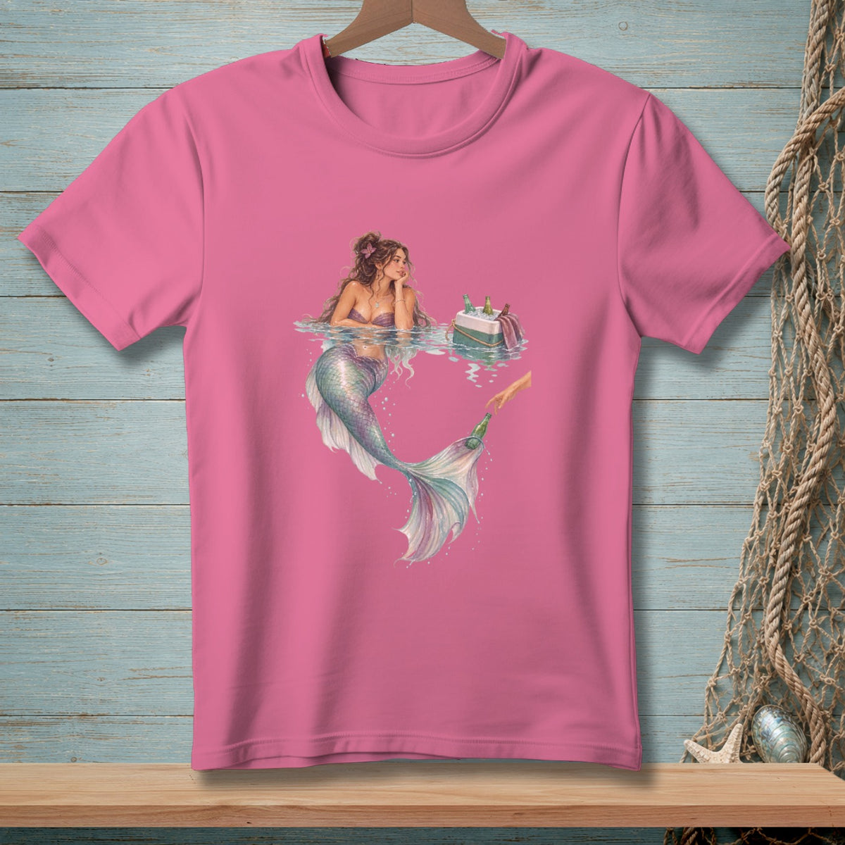 Pink t-shirt with a watercolor illustration of a mermaid relaxing by a cooler of drinks.