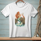 White t-shirt with a drawing of a mermaid holding a mirror, with a crab on a pier.