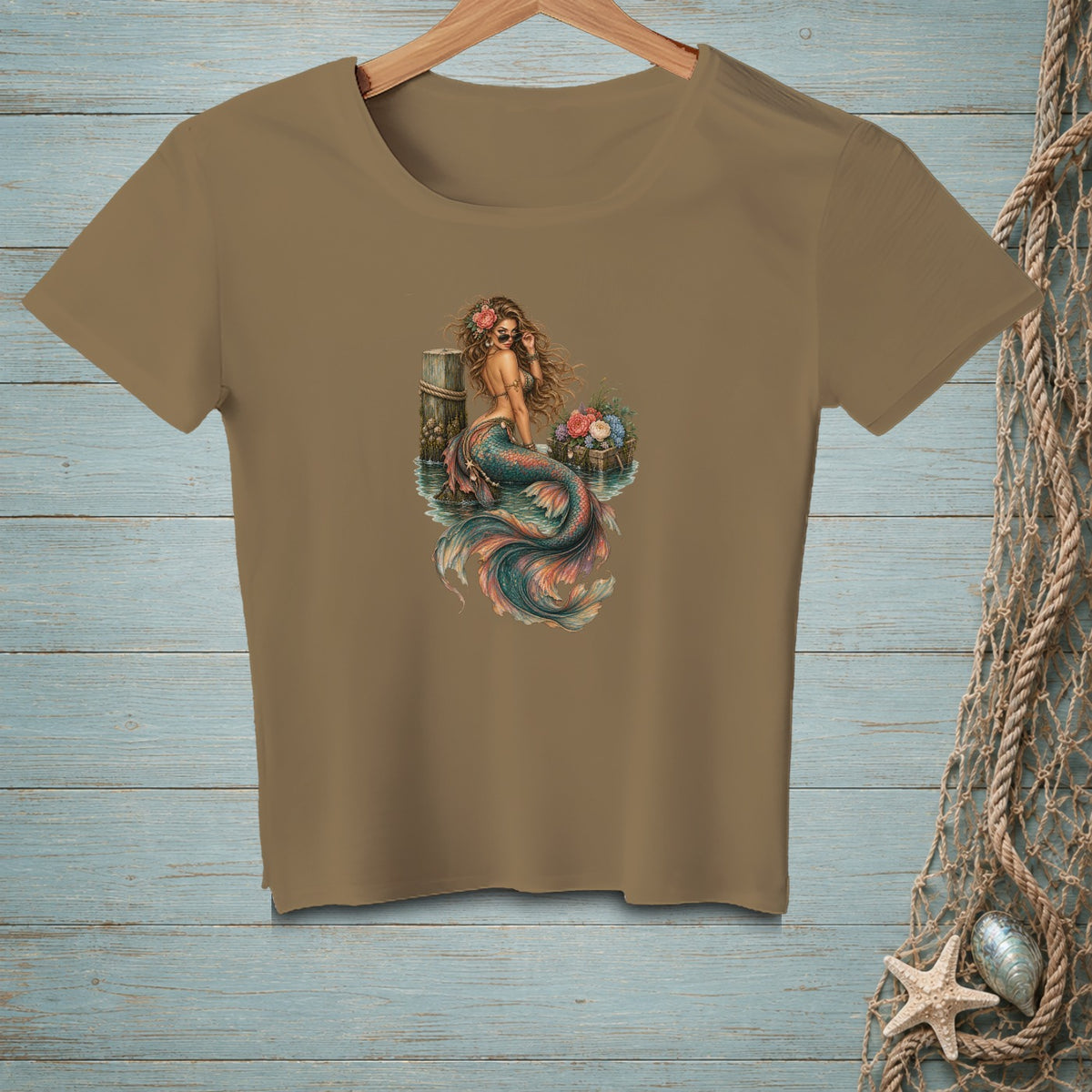 T-shirt with a tan base featuring a graphic of a mermaid sitting on a wooden post.