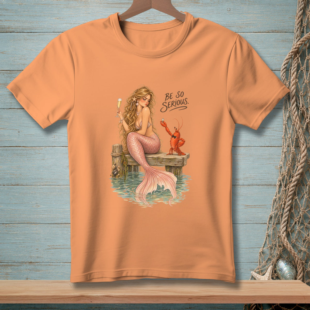 Peach t-shirt with a mermaid and lobster illustration and text "BE SO SERIOUS."
