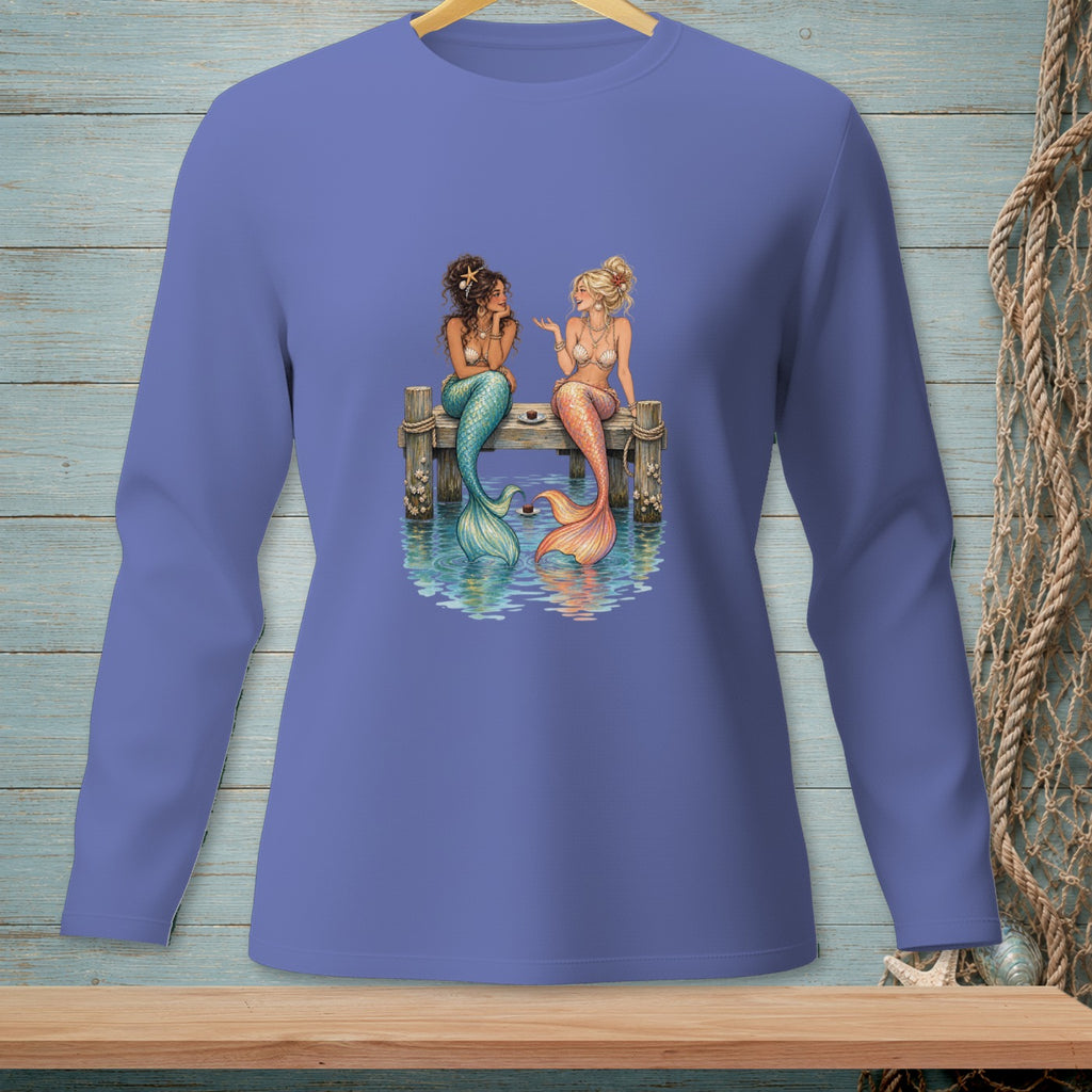 Two mermaids with colorful tails sit on a wooden pier talking.