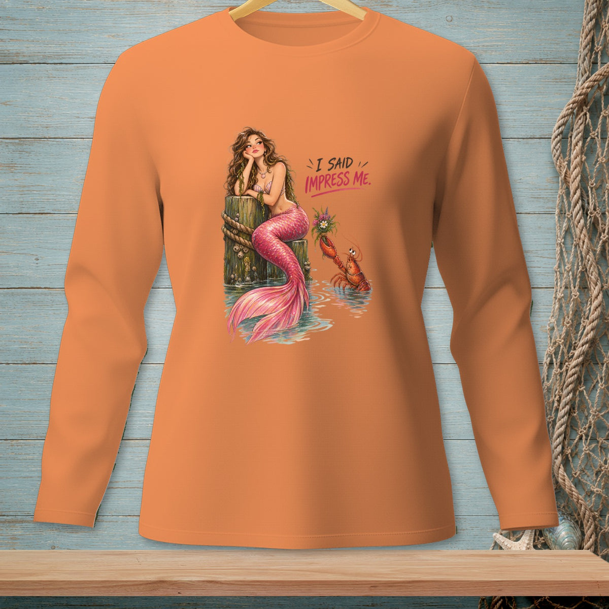 Orange long-sleeve shirt with a mermaid and lobster graphic saying "I said impress me."