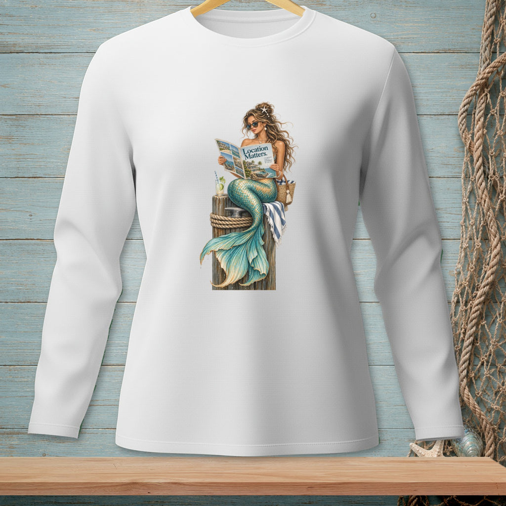 Long sleeve white shirt with a mermaid reading a magazine on a pier.