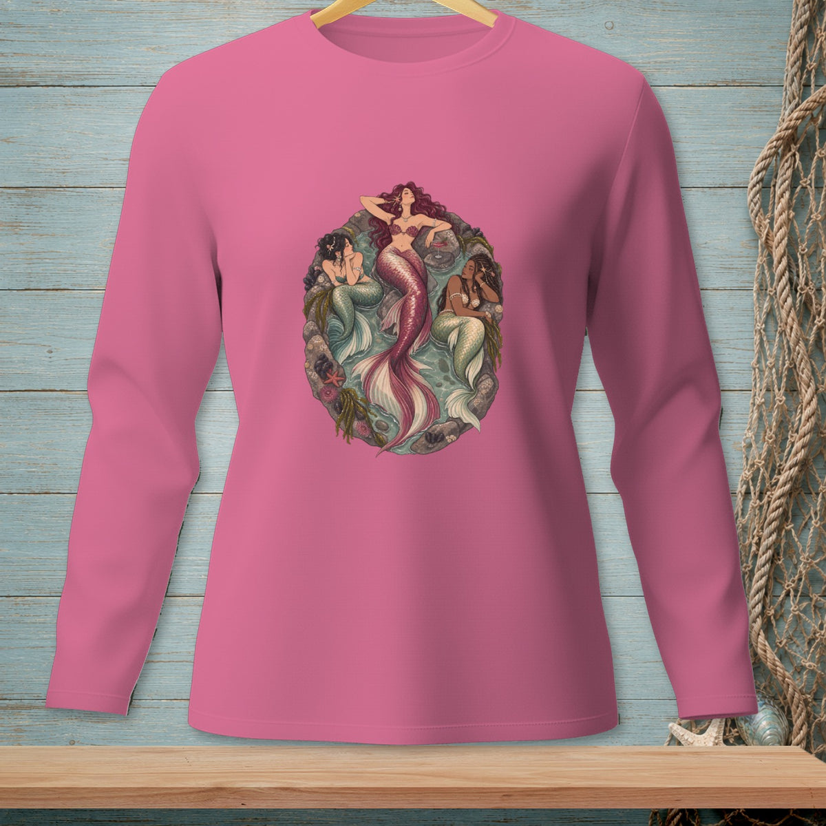 Pink long-sleeve shirt featuring three mermaids with detailed tails and seashell embellishments.
