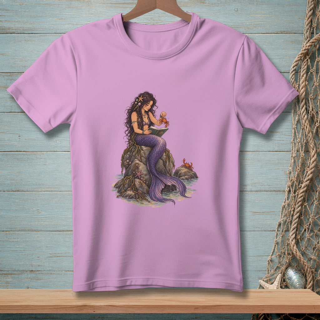 Mermaid sitting on rocks reading book with crabs nearby on pink t-shirt.