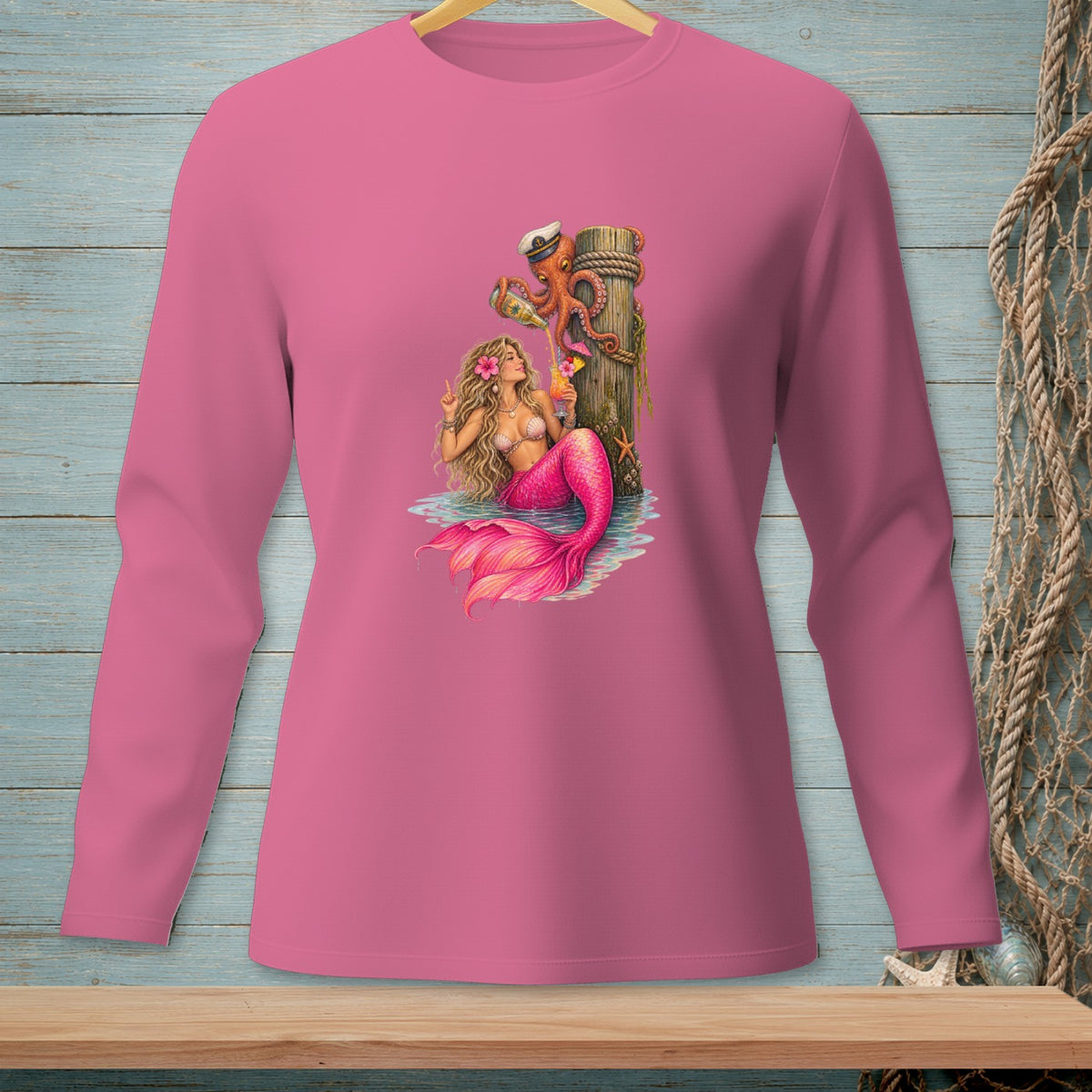 Pink long sleeve shirt with mermaid and octopus graphic enjoying drinks by a pier.