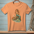 Peach t-shirt with mermaid, crab, and cocktail graphic on a rock.
