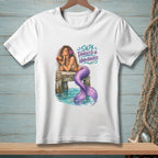 White t-shirt with a mermaid drinking a coconut on a dock, text "Salty, Tangled & Unbothered."